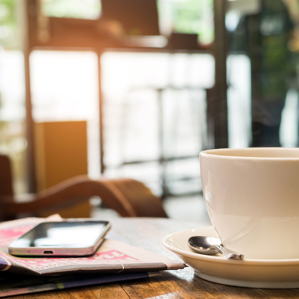 Coffee and a smart phone are on the newspaper.